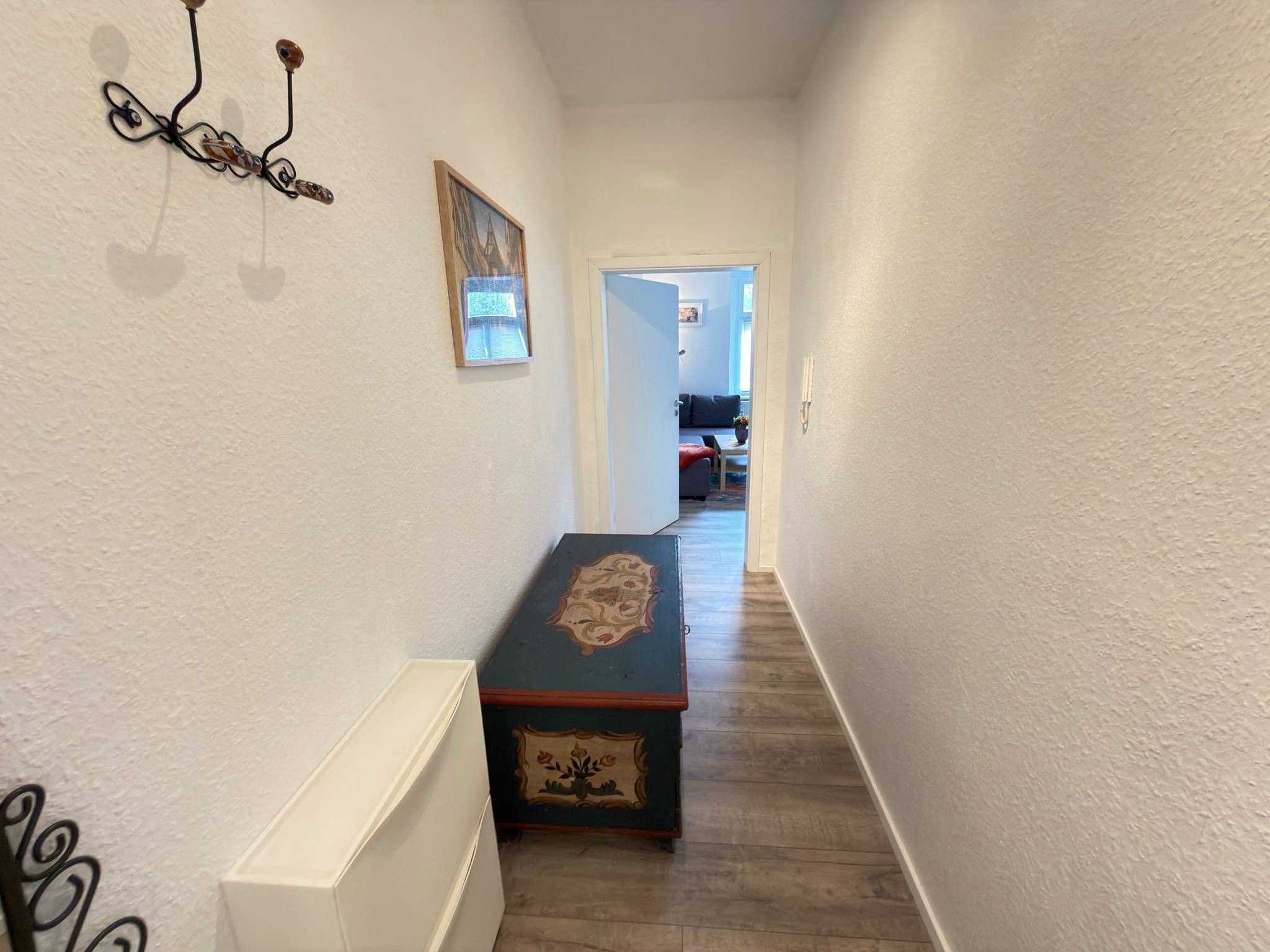 En smal gang med en radiator på venstre side, et pynteligt bord i midten og en døråbning til et andet rum.