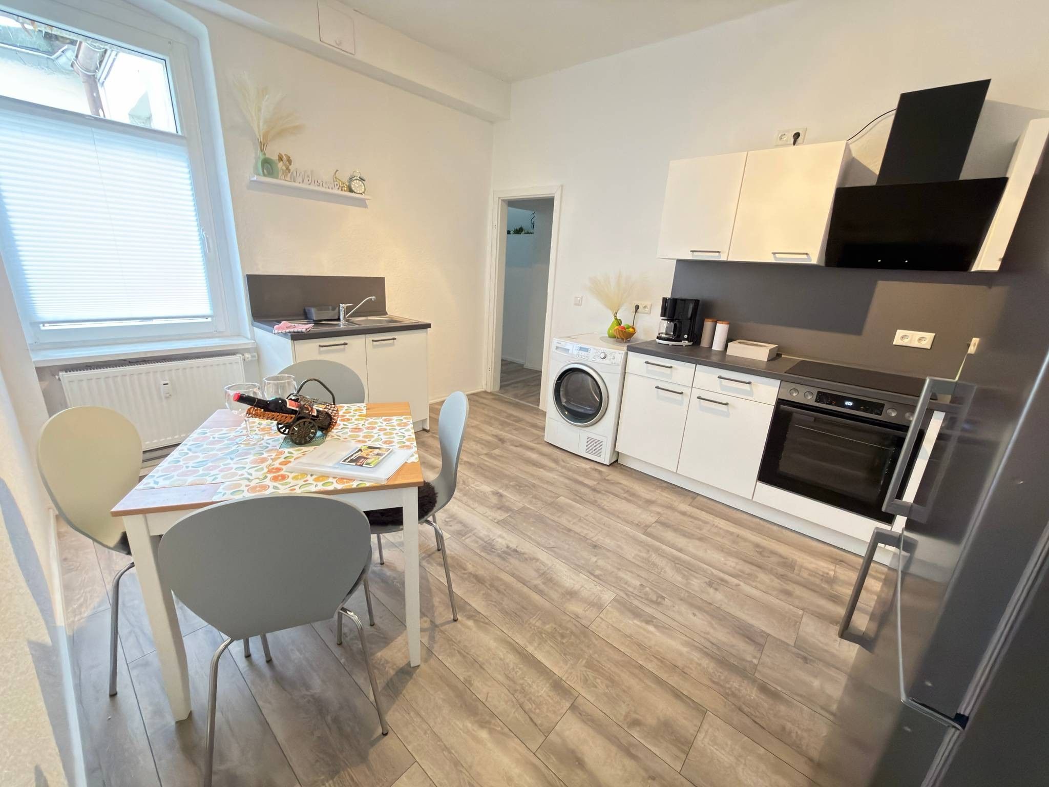 Et kompakt køkken med vaskemaskine, et spisebord med stole og et køleskab.