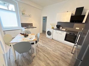 Et kompakt køkken med vaskemaskine, et spisebord med stole og et køleskab.