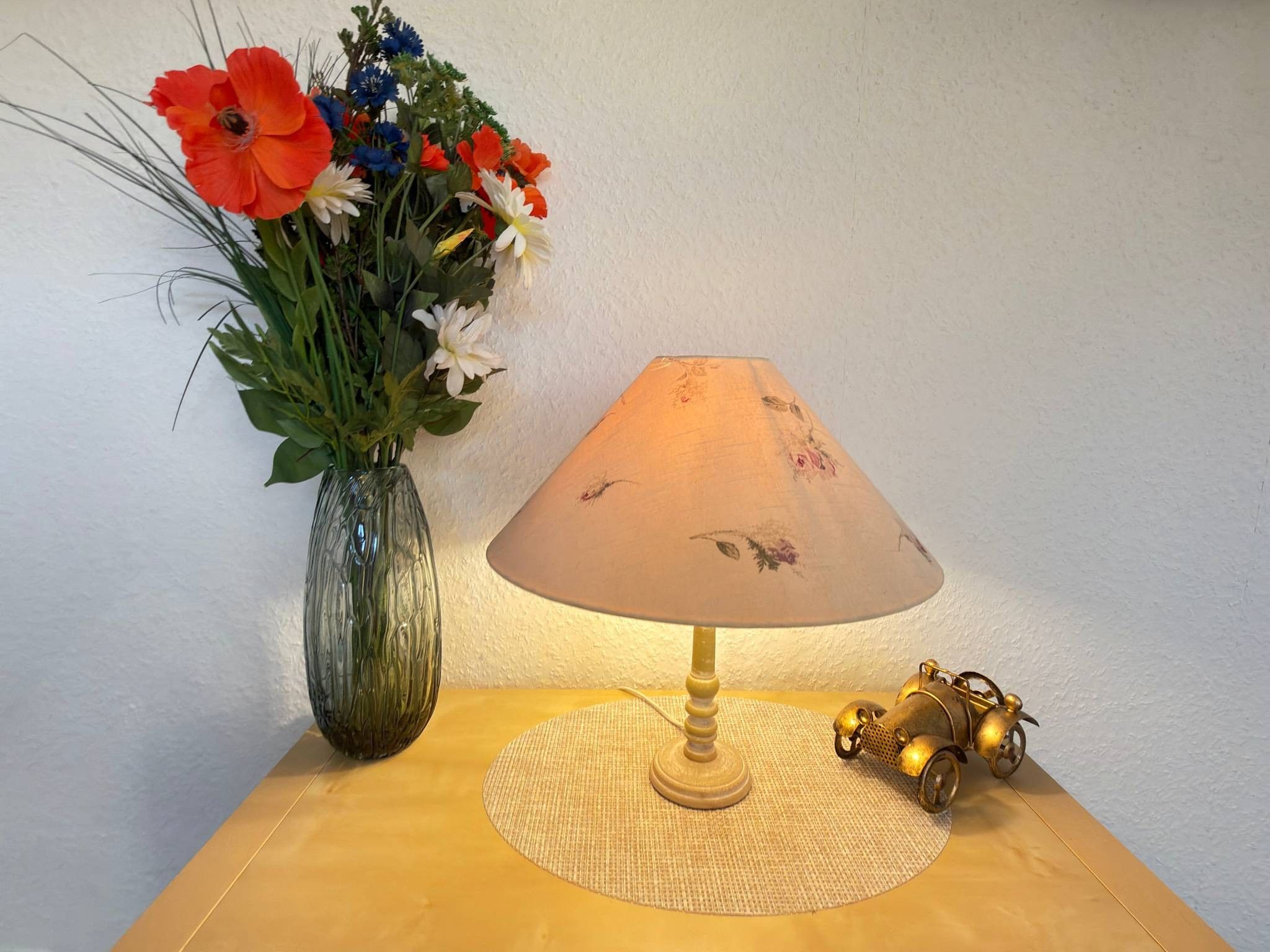 Een tafel met een lamp, een bloemenvaas en een decoratief object.