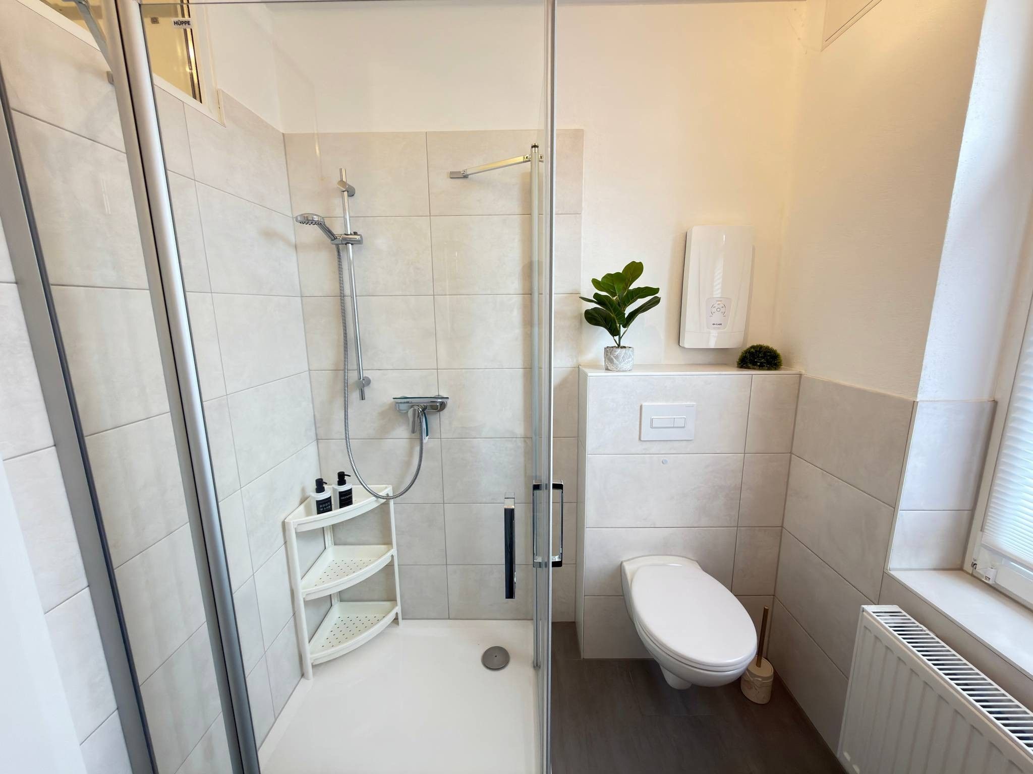 Ein modernes Badezimmer mit einer einteiligen Duschkabine, Toilette und einer kleinen Ablage für Pflegeprodukte.