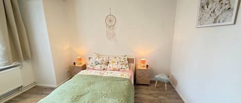 A bedroom with a bed, two bedside lamps, a dreamcatcher, a chair, and a wall-mounted picture.