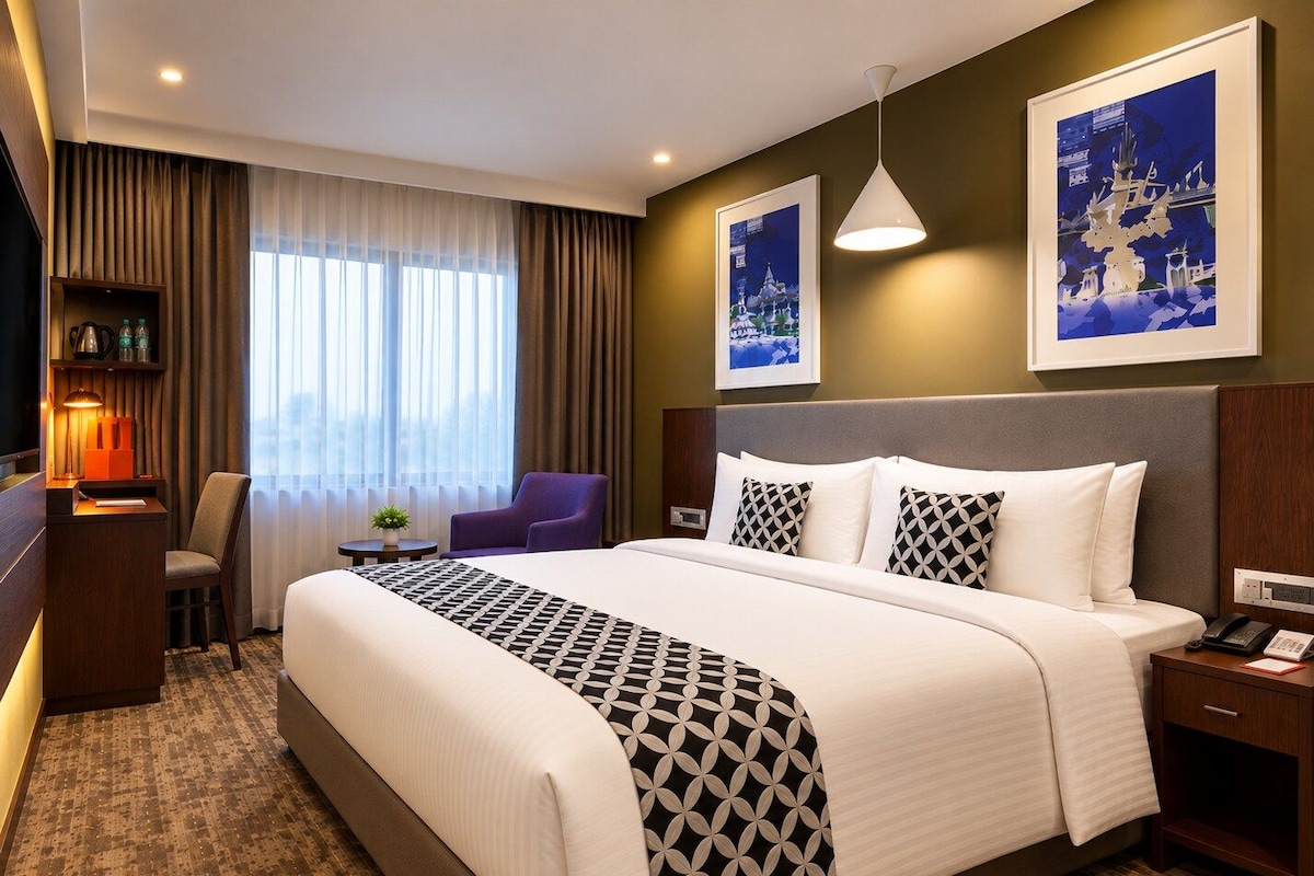 Ein Hotelzimmer mit einem großen Bett, einem Schreibtisch mit Lampe, einem Sessel und zwei gerahmten Bildern an der Wand.