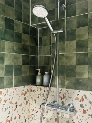 A bathroom with a shower, green tiles, and a soap dispenser. - S Homestay (Nghĩa Trụ)