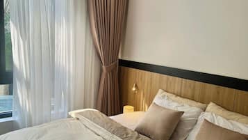 A neatly made bed with a magazine, a wooden headboard, and a window with sheer curtains.