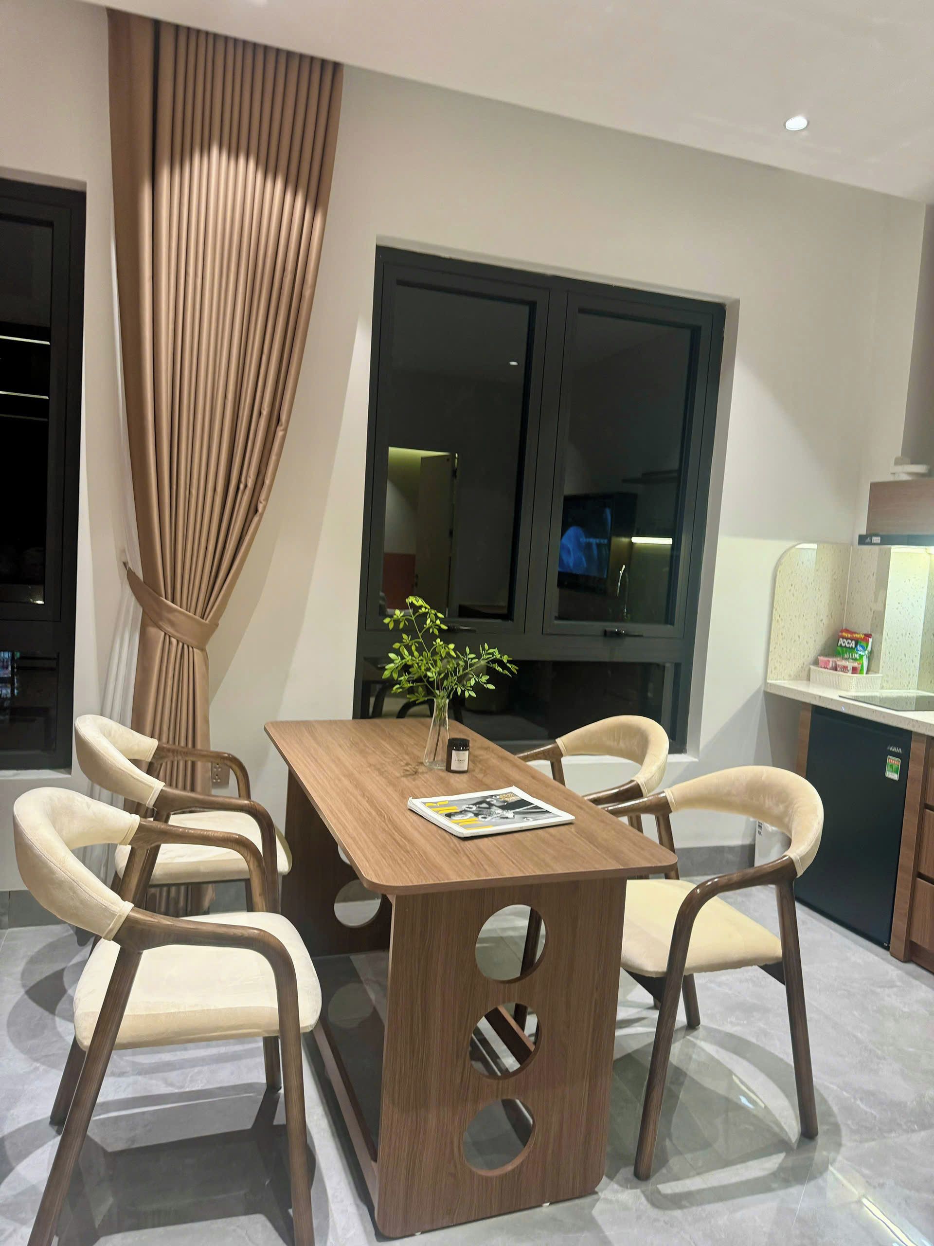 A modern dining area with a wooden table, six chairs, a vase with a plant, and a television in the background.