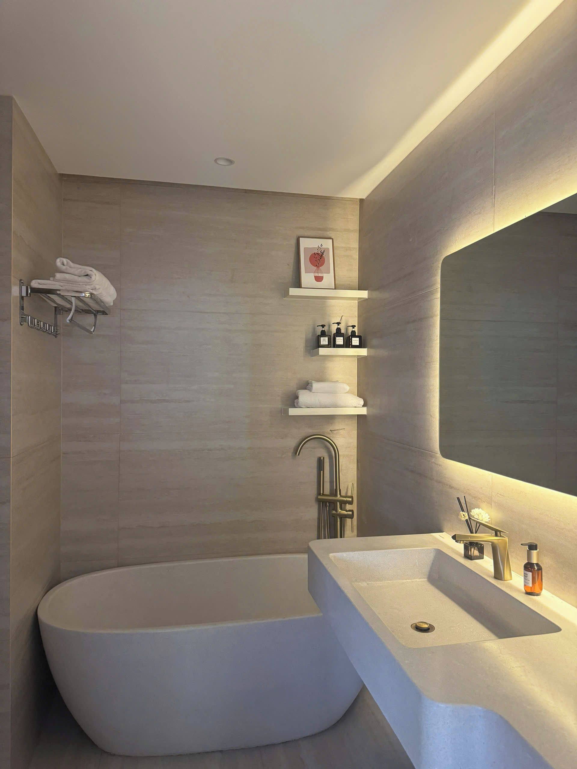 A modern bathroom with a freestanding bathtub, a large mirror, and built-in shelves with toiletries.