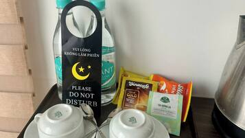 A tray with two white teacups, a teapot, a water bottle, and packets of snacks.