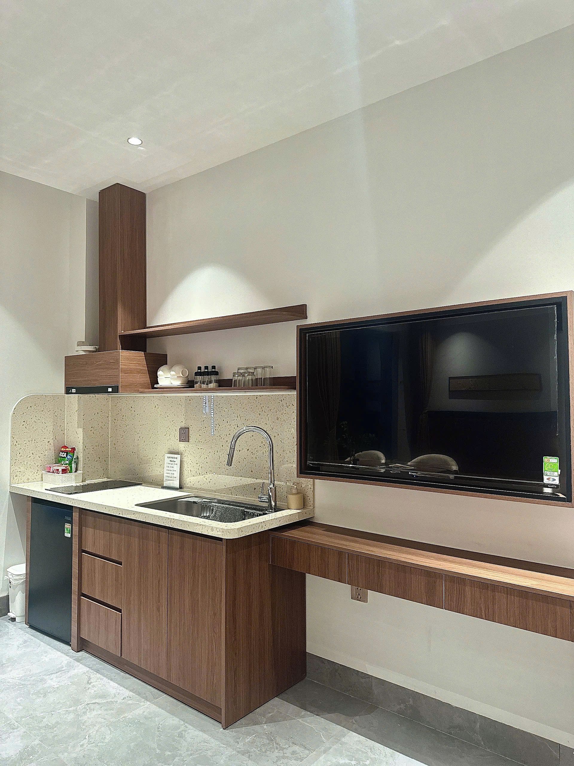 A modern kitchen with a built-in dishwasher, a stainless steel sink, and a large flat-screen TV mounted on the wall.