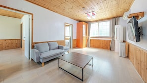 Et værelse med træloft, en grå sofa, et træbord og et stort vindue med gardiner.