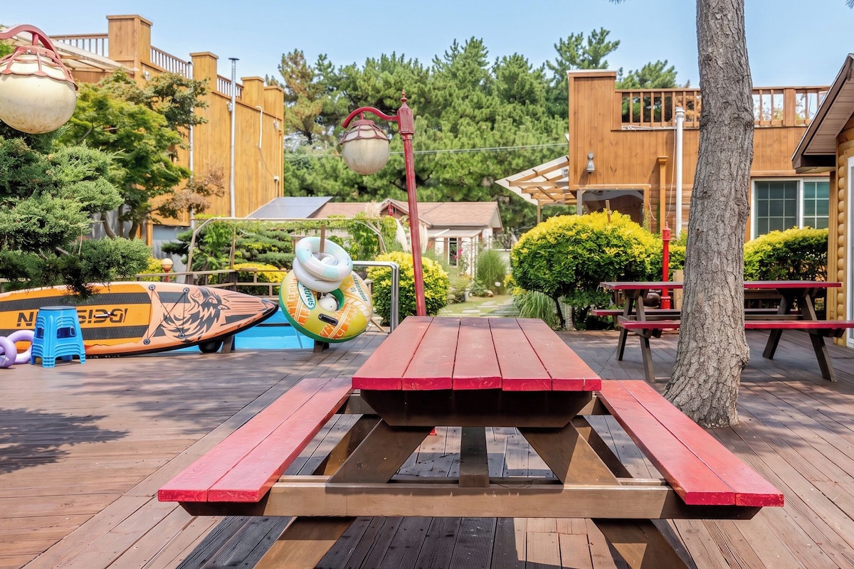 En træterrasse med et picnicbord, en pool og en træhytte.