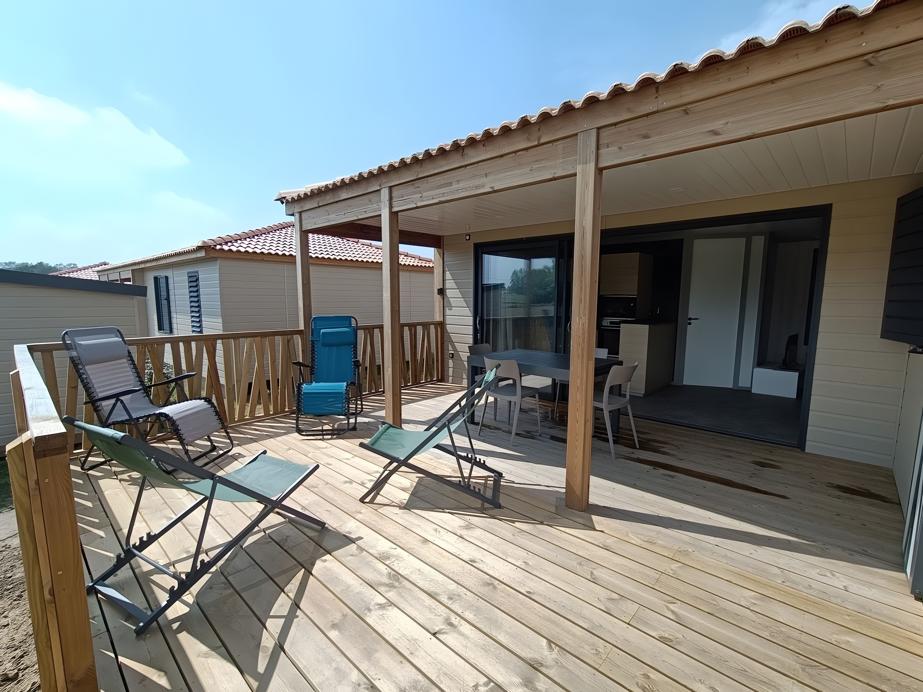 Een houten terras met lounge stoelen en een tafel, een overdekte patio en uitzicht op een gebouw met een pannendak.