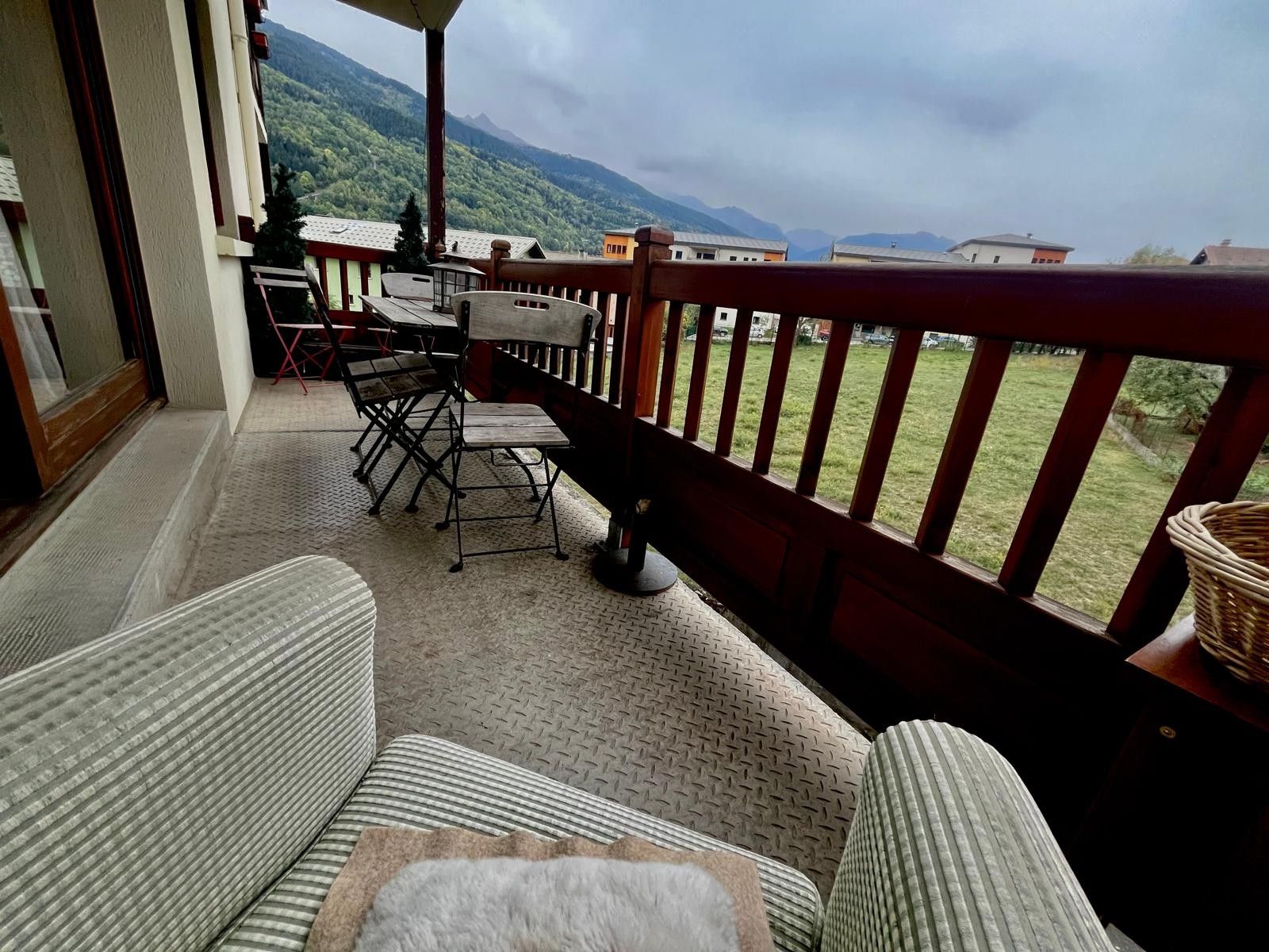 Een balkon met uitzicht op een bergachtig landschap, een tafel met stoelen en een rieten mand.