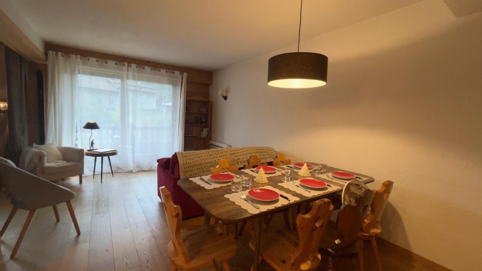 Een eethoek met een tafel voor vier personen, een rode bank, een lamp en een raam met gordijnen.