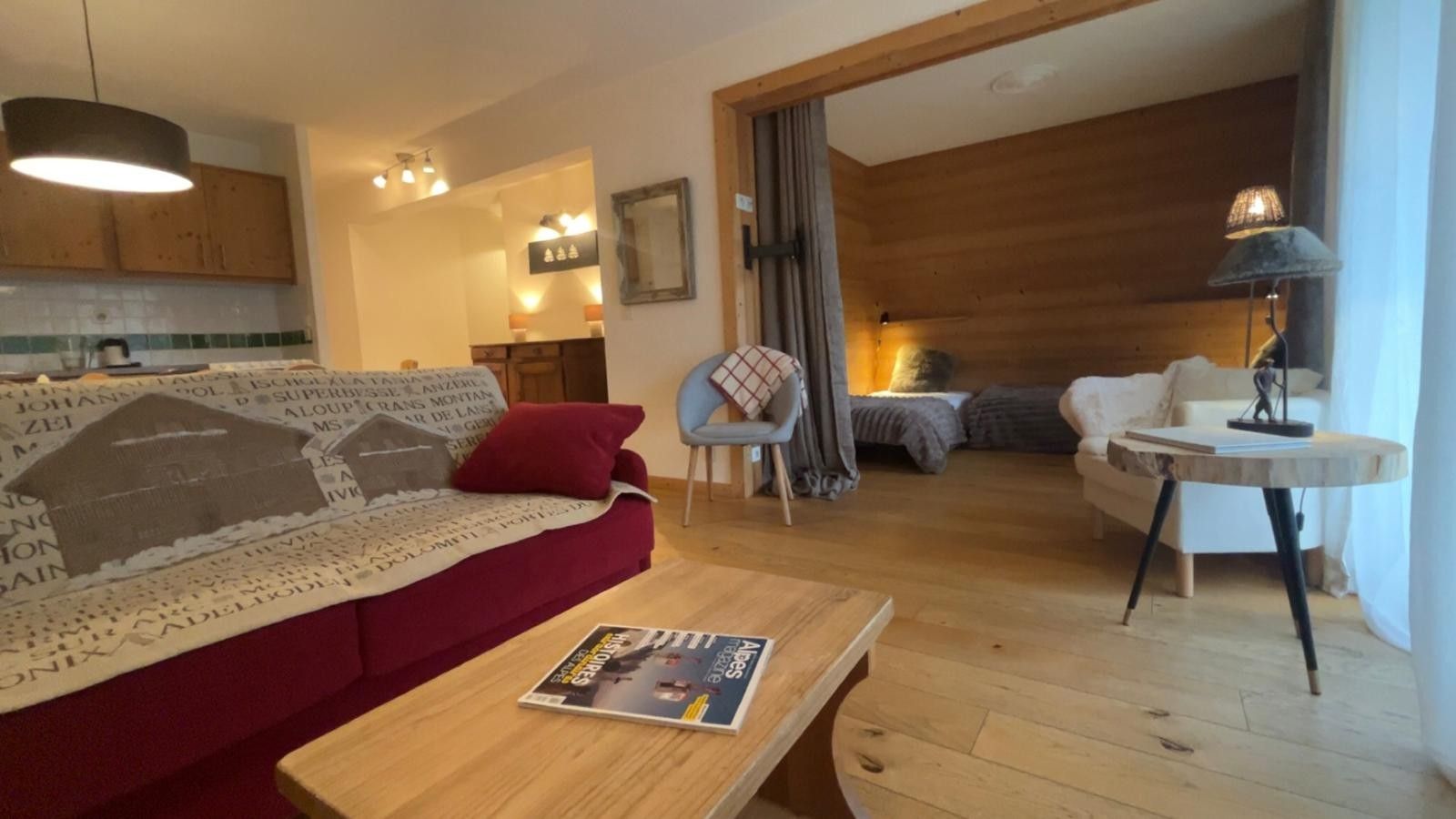 Een woonkamer met een rode bank, een houten salontafel en een eethoek met een ronde tafel en stoelen.
