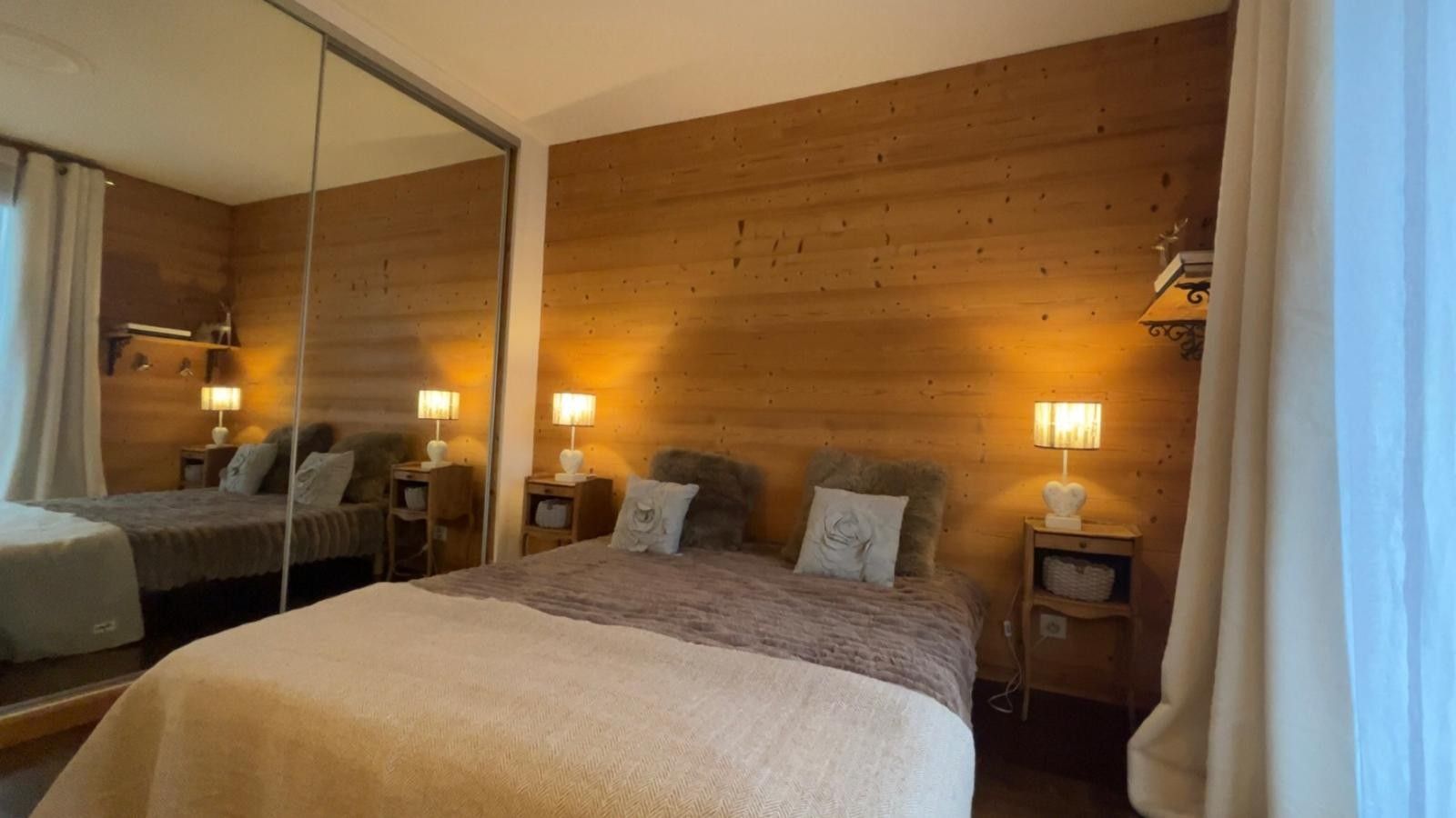 Una camera d'albergo con un letto grande, due comodini con lampade, uno specchio e pannelli di legno sulle pareti.
