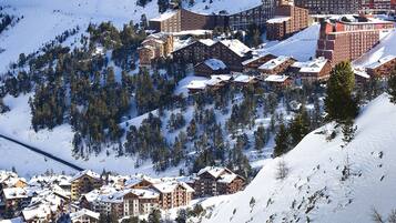 Een bergresort bedekt met sneeuw, met meerdere gebouwen, waaronder hotels en chalets, omgeven door bomen en skipistes.