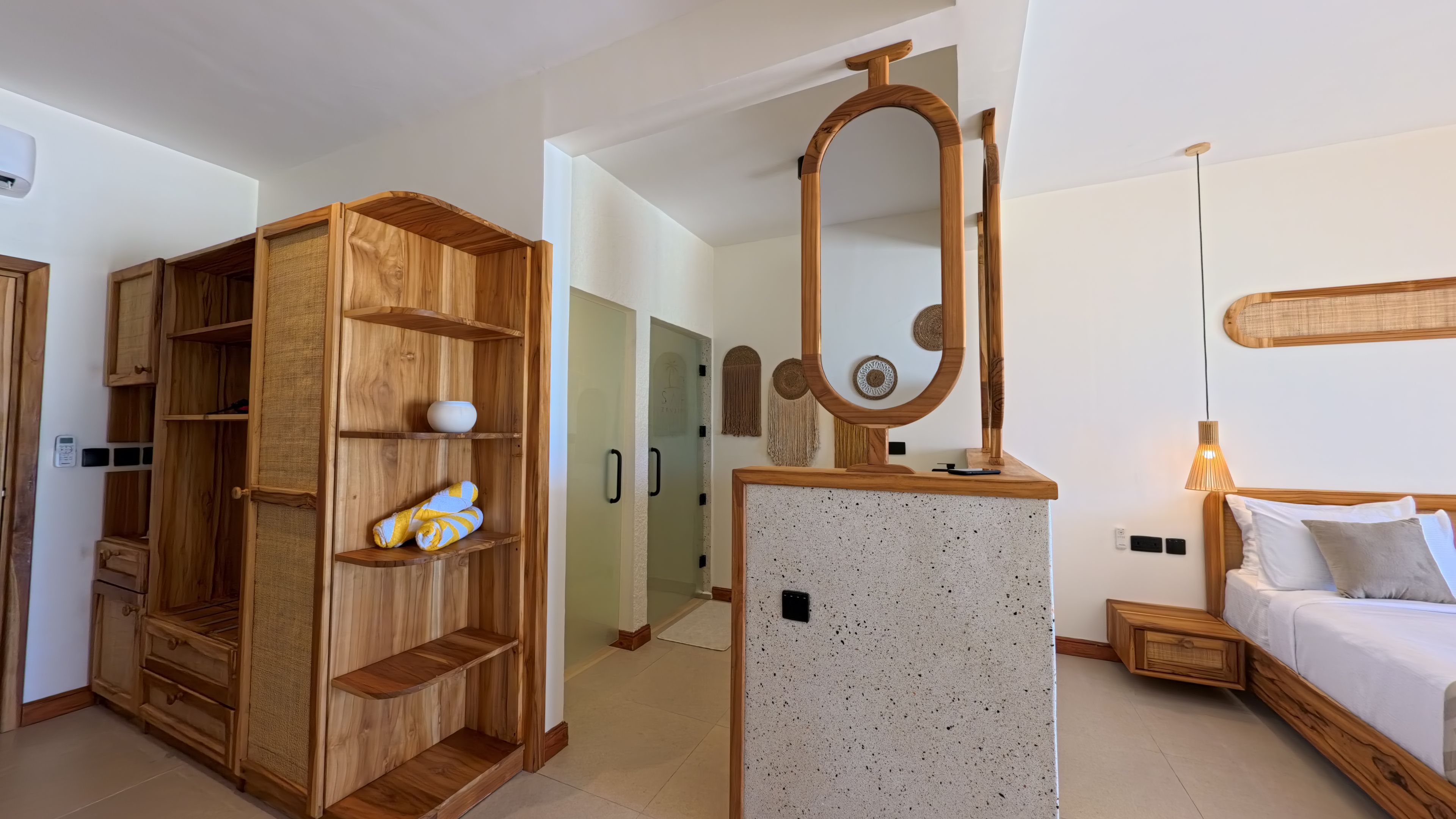 A modern room with a wooden wardrobe, a mirror, a bed with white bedding, and a small bedside table.