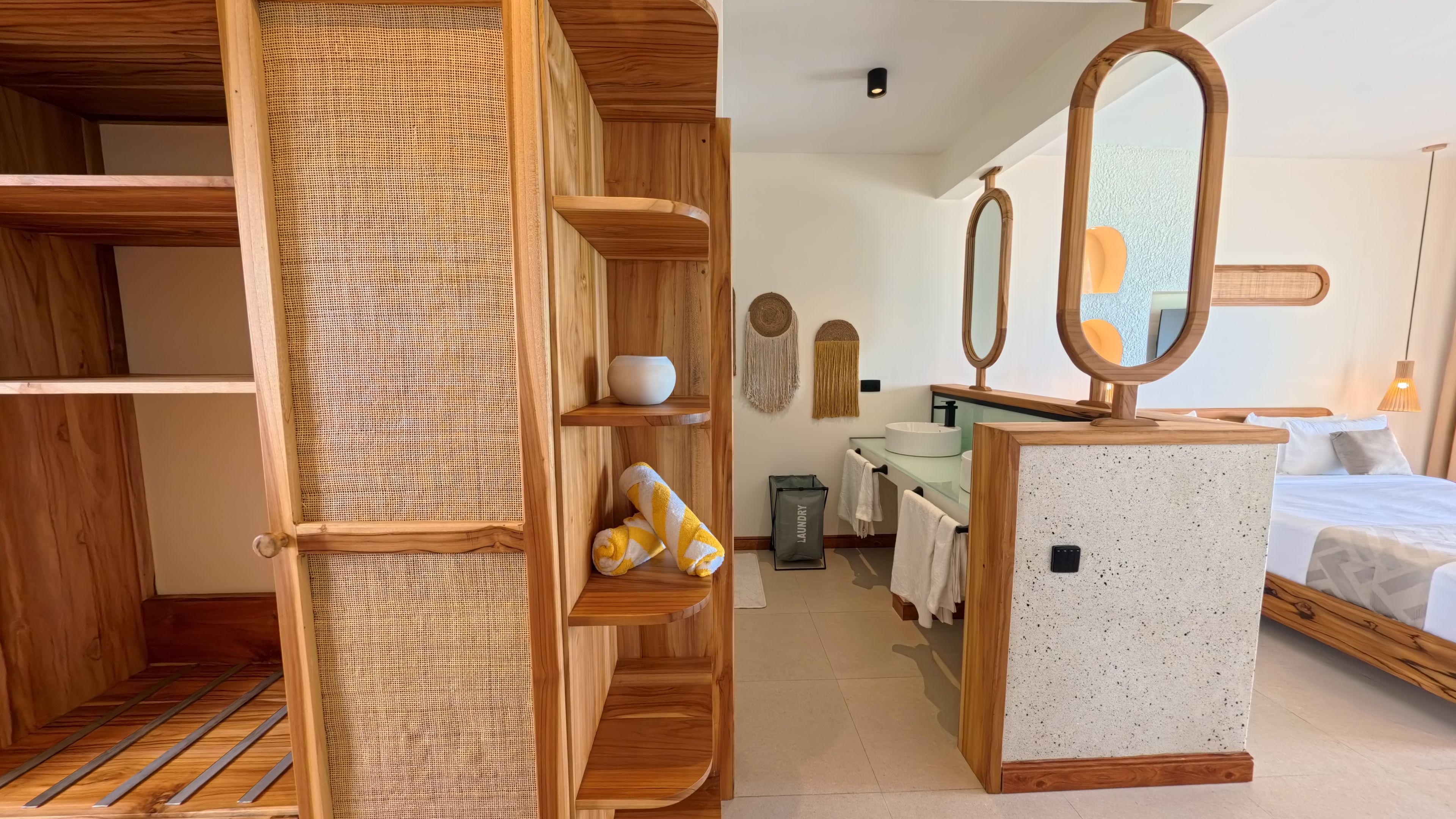 Habitación de hotel con armario de madera, cama, baño con espejo y una bolsa para la ropa.