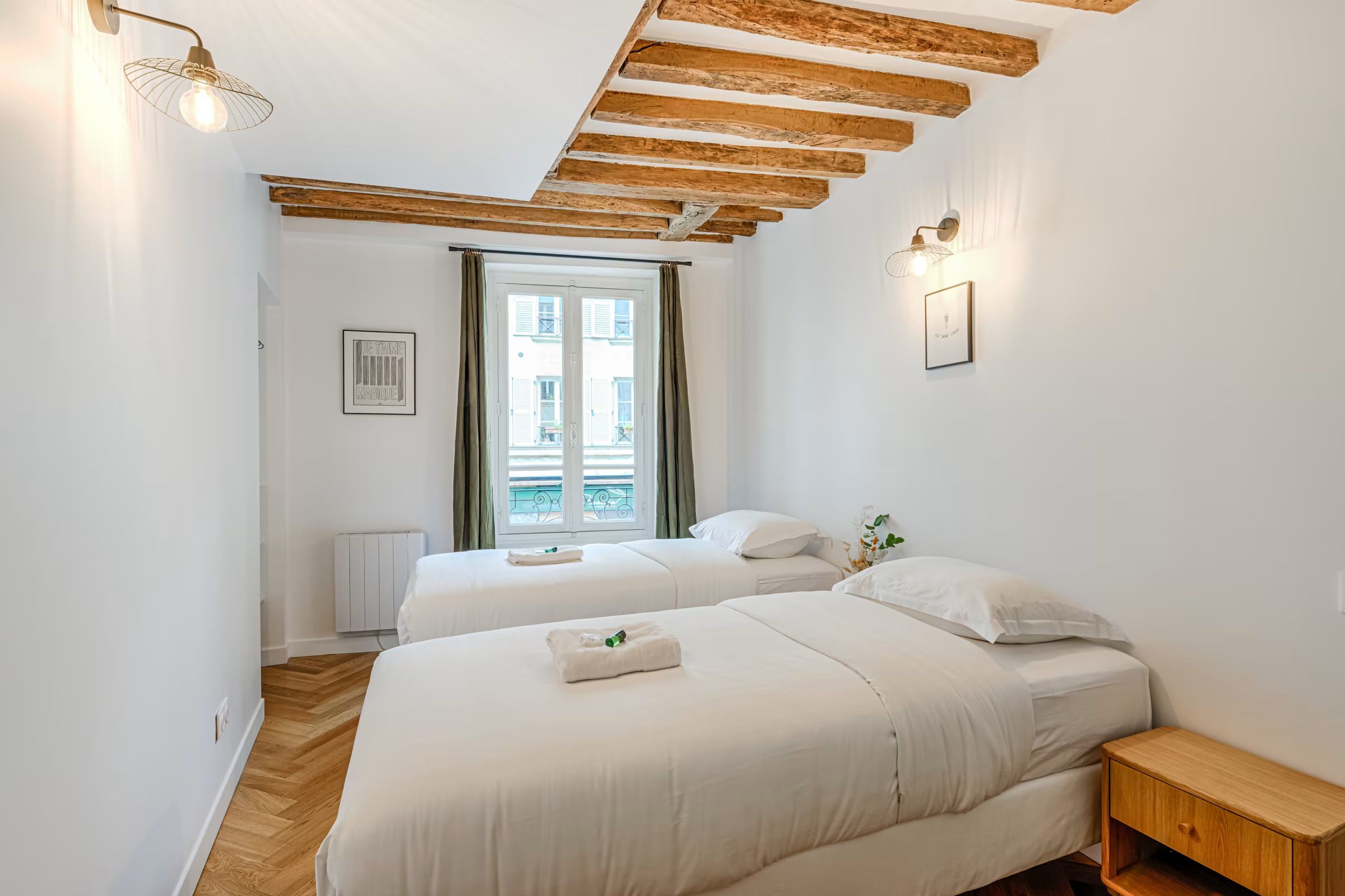 Una habitación de hotel con dos camas, techo de madera, ventana con cortinas y un radiador.