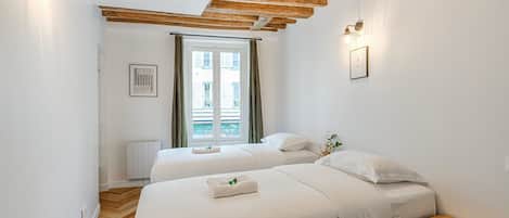 Una habitación de hotel con dos camas, techo de madera, ventana con cortinas y un radiador.