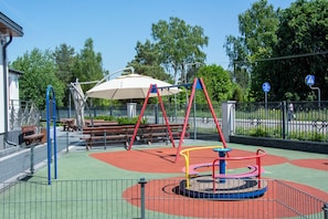 Un parque infantil con columpios, una mesa y un área de descanso techada.