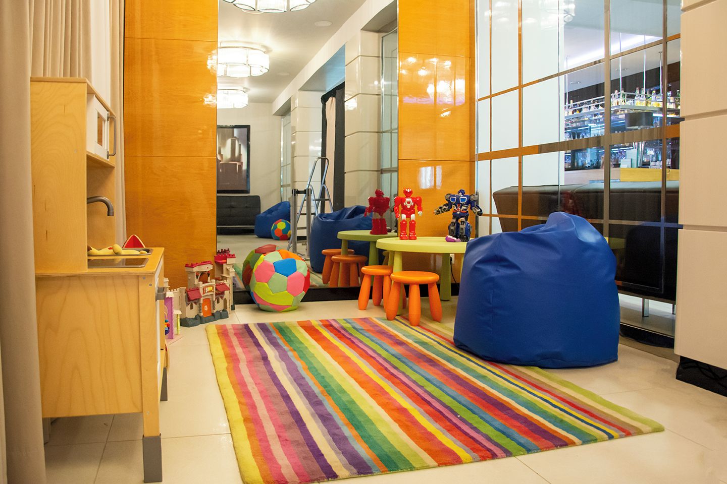 Espaço de recreação infantil com brinquedos coloridos, um tapete listrado em arco-íris e sacos de feijão.