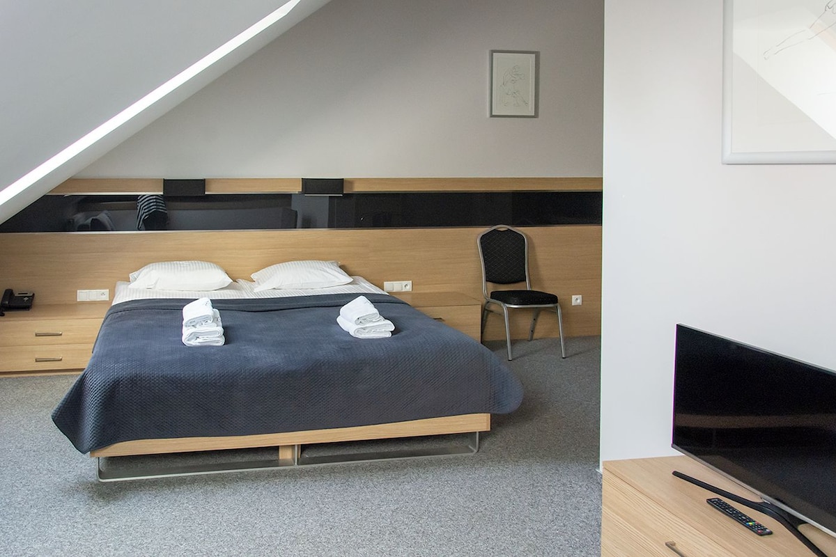 A modern hotel room with a bed, a chair, a desk, and a television.