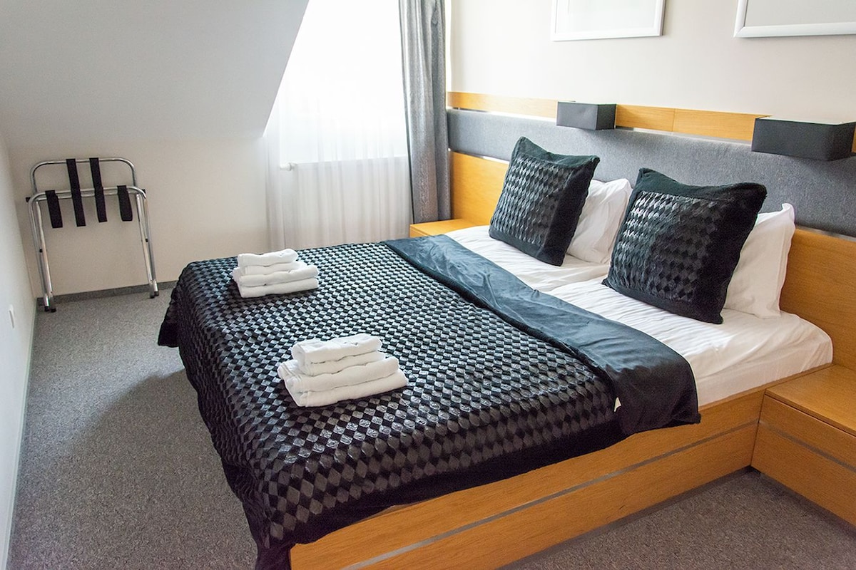A hotel room with a bed, pillows, a blanket, and a towel rack.