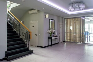 Un interior moderno con una escalera, una consola con un florero y un ventanal con cortinas.