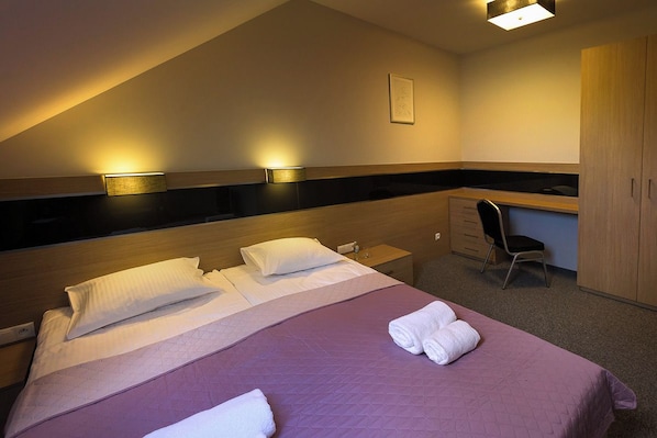 Una habitación de hotel con una cama, un escritorio, una silla y un armario.
