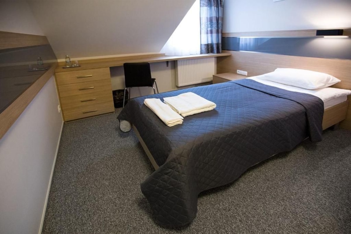 A bedroom with a bed, a desk, a chair, and a radiator.