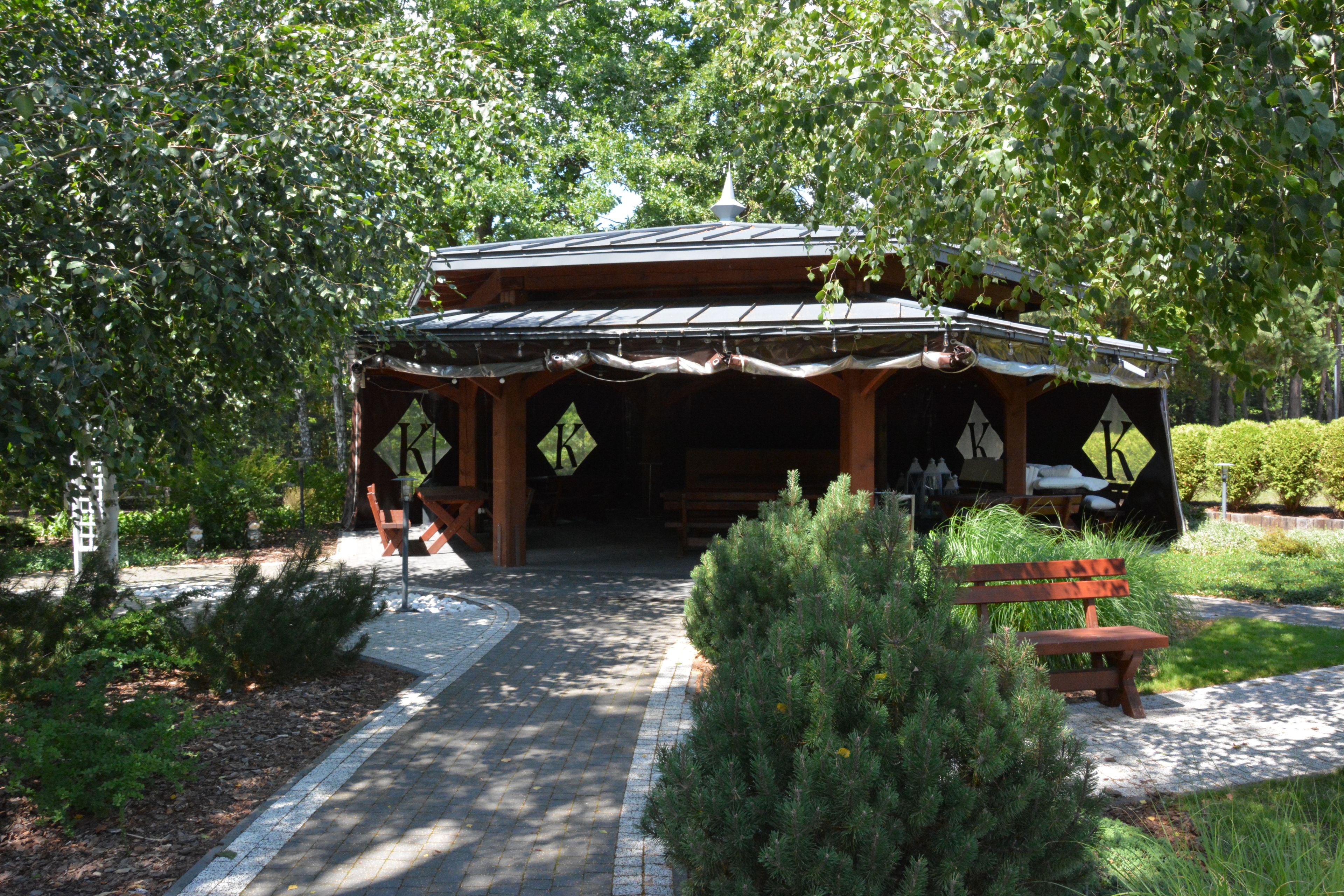 Une construction traditionnelle en bois, surmontée d’un toit de tuiles, entourée d’une végétation luxuriante et accessible par un chemin pavé.