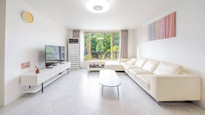 Uma sala de estar moderna com televisão de tela plana, sofá, mesa de centro e varanda com vista para o verde.