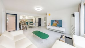 Uma sala de estar moderna com um sofá, um banquinho verde, uma TV de tela plana e um aparelho de ar condicionado branco.