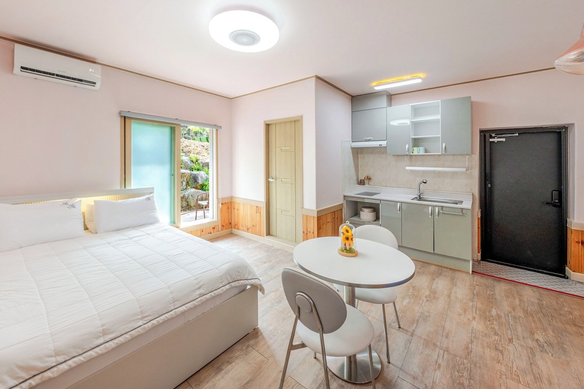 Quarto compacto com cama, mesa pequena para refeições com cadeiras, cozinha compacta e porta para área externa.
