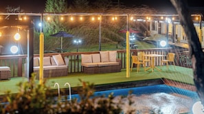 Área de estar ao ar livre com piscina, assentos e luzes de corda.