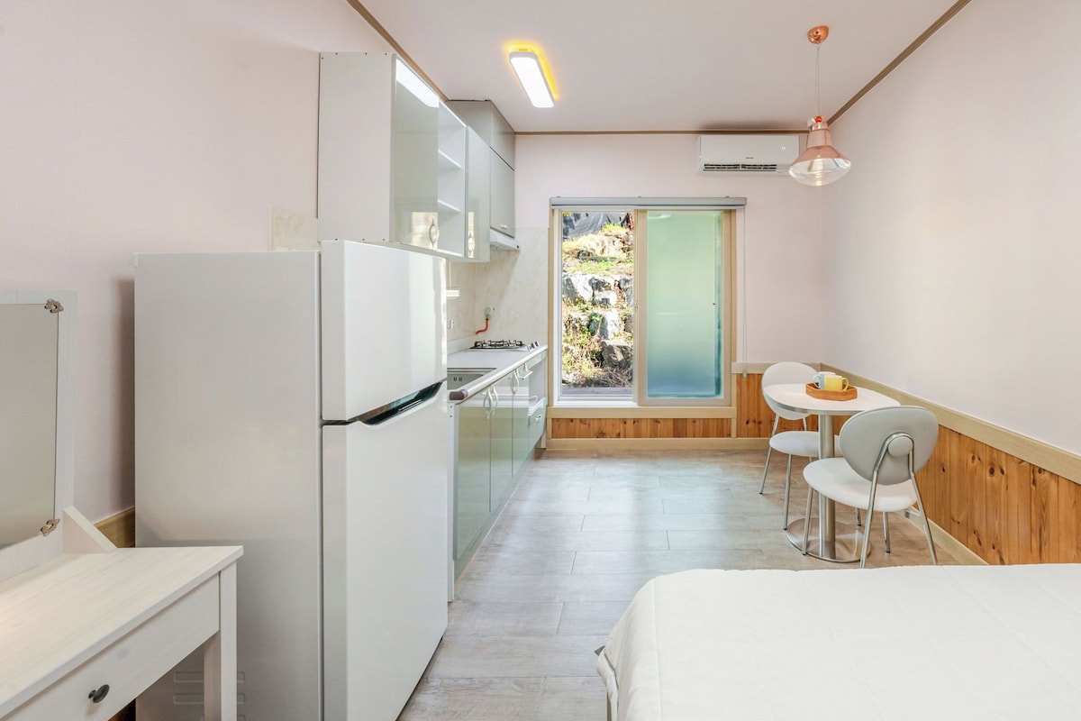 Quarto de hotel compacto com cozinha americana, área de refeições e uma cama.