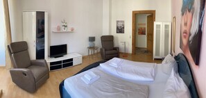 Ein Hotelzimmer mit einem Bett, zwei Sesseln, einem Fernseher, einem kleinen Tisch und einem Kleiderschrank.