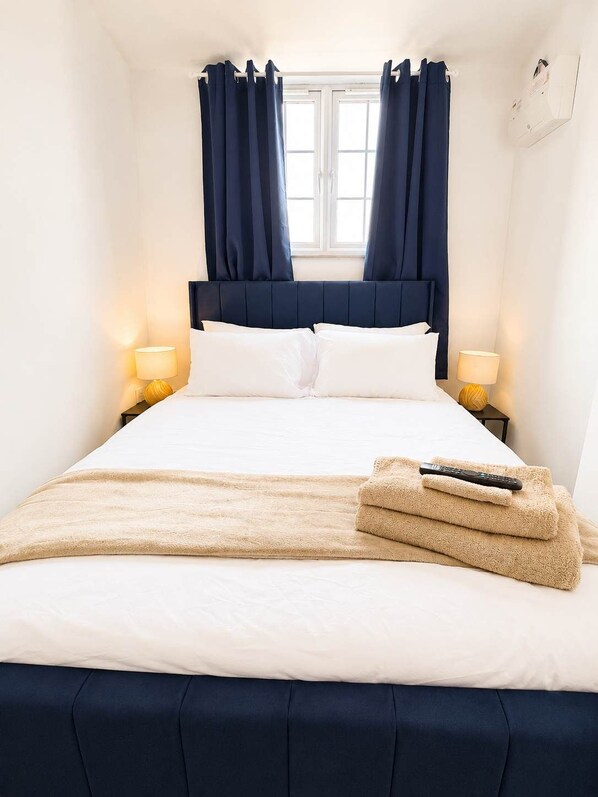 Een hotelkamer met een bed, twee bedlampen, een raam met gordijnen en een afstandsbediening op het bed.