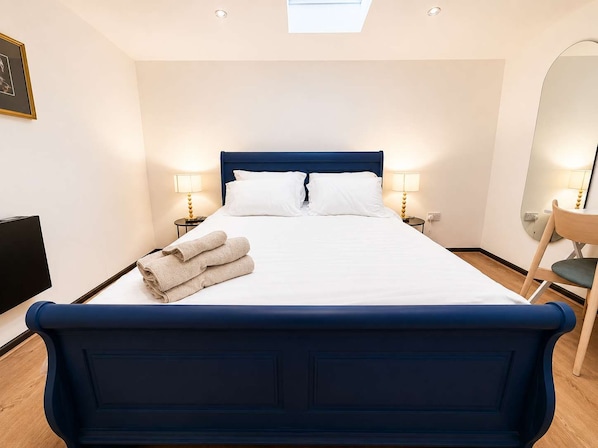 A neatly made bed with a blue headboard, two bedside lamps, and a pair of folded towels on the bed. - Modern 2 Bed Flat in Heart of Warrington City (Warrington)