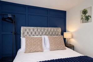 A bedroom with a tufted headboard, two pillows, a bedside lamp, and a wall-mounted plant. - Modern house-4 Bed - Close to Motorway & Town, (Warrington)