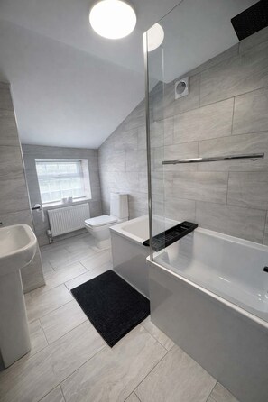 Ein modernes Badezimmer mit einer begehbaren Glasdusche, einer weißen Badewanne und einem WC.