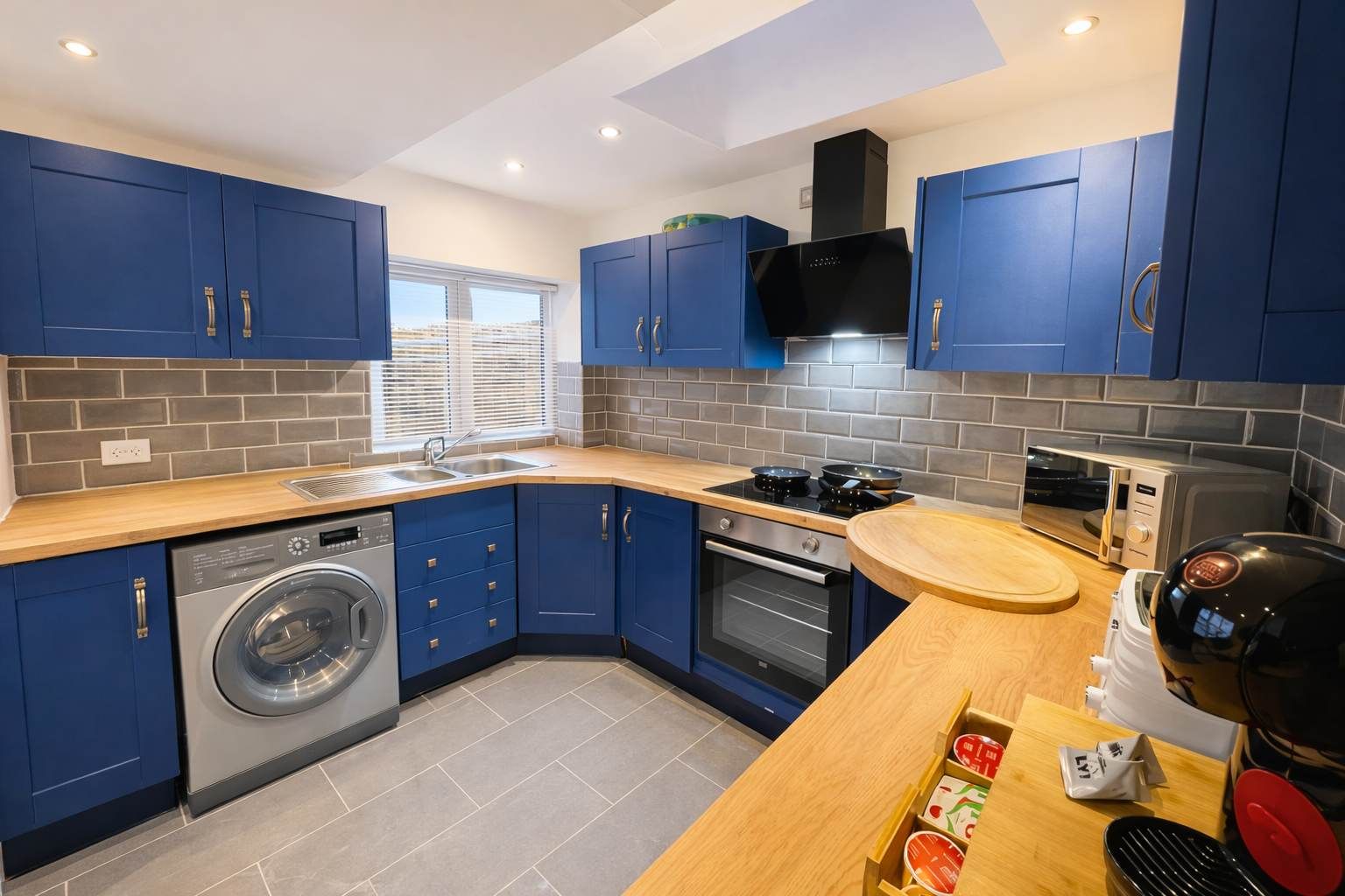 Een moderne keuken met blauwe kastjes, een inbouwoven, een magnetron en een vaatwasser.