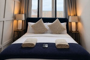 A hotel room with a bed, two pillows, two bedside lamps, and a remote control on the bed. - Modern 2 Bedroom Apartment in Central Warrington (Warrington)