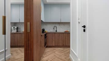 A hallway view looks directly into a modern kitchen area. The warm wood tones of the lower cabinets and the light herringbone-patterned floor create a welcoming entryway.