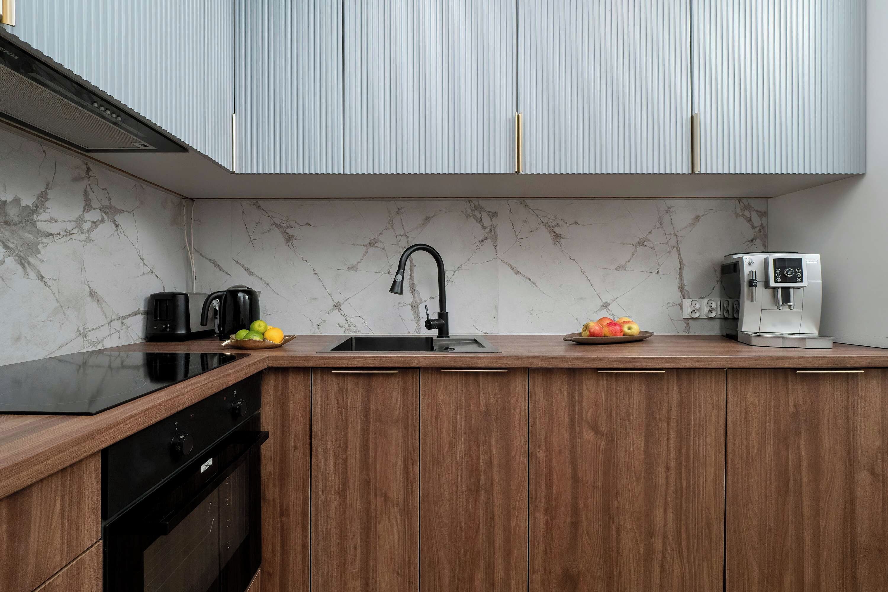Cozinha moderna com painel de parede em mármore, armários de madeira, fogão preto, pia e cafeteira.