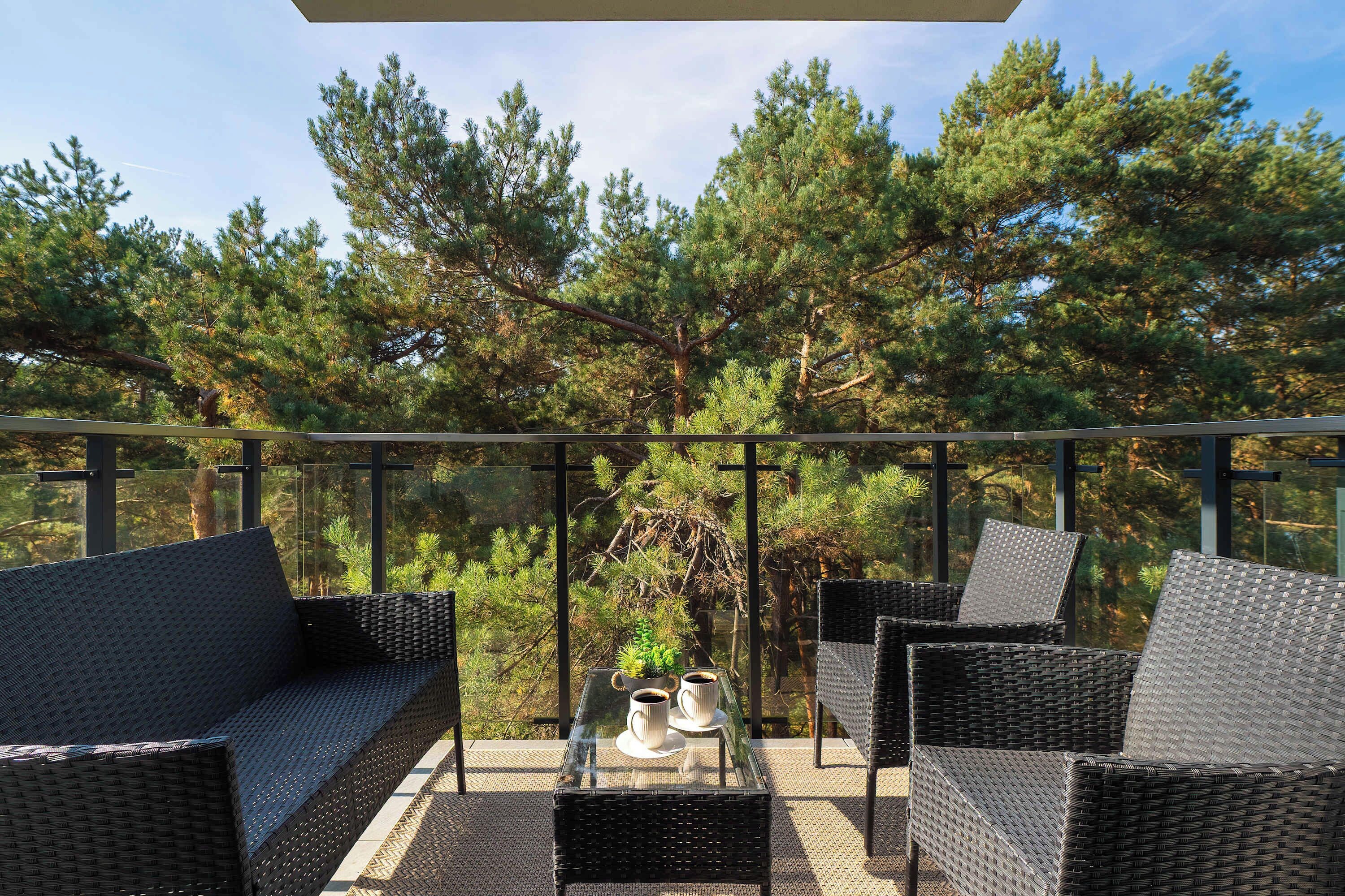 A balcony with wicker furniture, a glass table, and a potted plant.