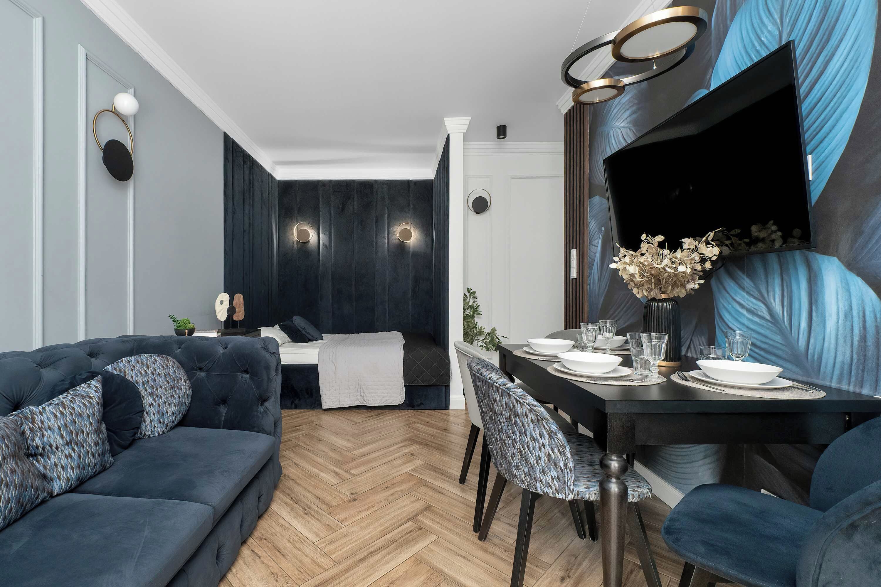 Un soggiorno moderno con un divano blu scuro, un'area pranzo con tavolo e sedie nere, e un grande televisore piatto montato a parete.