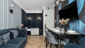 Un soggiorno moderno con un divano blu scuro, un'area pranzo con tavolo e sedie nere, e un grande televisore piatto montato a parete.